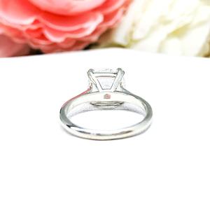 Sterling silver engagement ring with a sparkling cushion cut lab created white sapphire set in a split-prong setting set against a white surface with soft-focus pink and white flowers in the background.