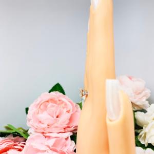Mannequin hand with long white shimmery nails, displayed against a soft white-gray background with pink and white floral accents. The hand is wearing a sterling silver split prong cathedral engagement ring set with an 7.5mm near colorless old mine cut cubic zirconia.