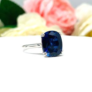 Sterling silver ring featuring a vivid elongated cushion-cut lab created blue sapphire held in a split-prong setting, with soft-focus pink and white flowers in the background.