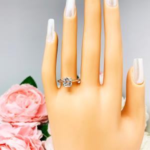 Mannequin hand with long white shimmery nails, displayed against a soft white-gray background with pink and white floral accents. The hand is wearing a sterling silver split prong cathedral engagement ring set with an 7.5mm near colorless old mine cut cubic zirconia.