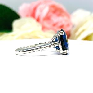 Sterling silver ring featuring a vivid elongated cushion-cut lab created blue sapphire held in a split-prong setting, with soft-focus pink and white flowers in the background.