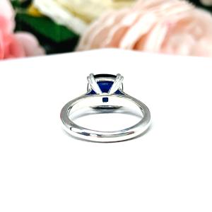 Close-up of a sterling silver cathedral-style ring featuring an 8mm cushion cut lab created blue sapphire center stone.  The ring is facing toward the back to display the prongs and polished band.
