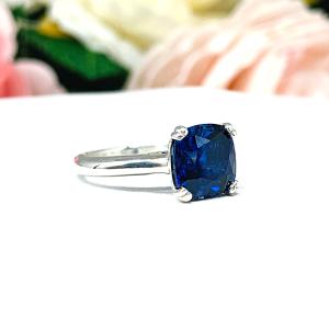 Close-up of a sterling silver cathedral-style ring featuring an 8mm cushion cut lab created blue sapphire center stone. The ring is facing slightly to the right to showcase the mixed brilliant faceting and highly polished band.