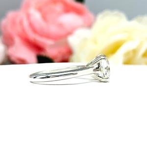 A sterling silver split-prong cathedral engagement ring set with a near colorless old mine cut cubic zirconia. The ring is set against a white background with a blurred image of pink and white flowers in the background.