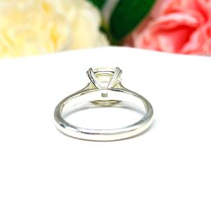 Sterling silver split prong cathedral engagement ring set with an 8mm light yellow old mine cut cubic zirconia. The ring is resting on a white surface with a background of pink and white flowers.