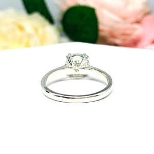 Close-up view of a near colorless (G/H color) round brilliant cut cubic zirconia solitaire ring in a split prong cathedral setting. The ring is made of sterling silver and features a sleek, minimalist design. The setting is simple yet elegant, allowing the center stone to take center stage. The ring is displayed against a soft, blurred background of pastel-colored flowers, creating a romantic and delicate ambiance.