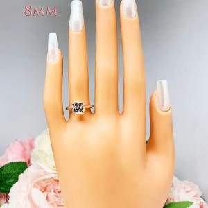 Mannequin hand with long white shimmery nails, displayed against a soft white-gray background with pink and white floral accents. The hand is wearing a sterling silver ring with a sparkling cushion cut lab created white sapphire set in a split-prong setting. The text '8MM' appears in the image.