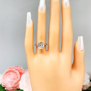Mannequin hand with long white shimmery nails, displayed against a soft white-gray background with pink and white floral accents. The hand is wearing a sterling silver split-prong cathedral engagement ring set with a near colorless old mine cut cubic zirconia. The text '9MM' appears in the image.