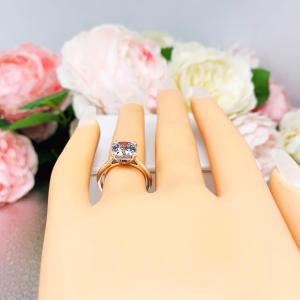Mannequin hand with long white shimmery nails, displayed against a soft white-gray background with pink and white floral accents. The hand is wearing a sterling silver split-prong cathedral engagement ring set with a colorless old mine cut cubic zirconia.