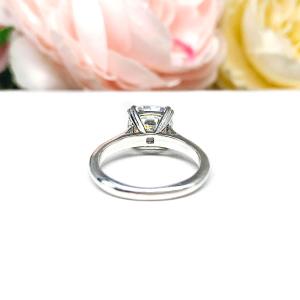 A sterling silver split-prong cathedral engagement ring set with a colorless old mine cut cubic zirconia. The ring is set against a white background with a blurred image of pink and white flowers in the background.