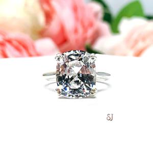 Sterling silver engagement ring featuring a sparkling elongated cushion-cut lab created white sapphire held in a split-prong setting, with soft-focus pink and white flowers in the background.