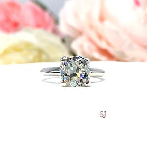 Sterling silver engagement ring set with an 8mm old mine cut near colorless cubic zirconia. The ring is resting on a white surface with a background of soft-focus pink and white flowers.