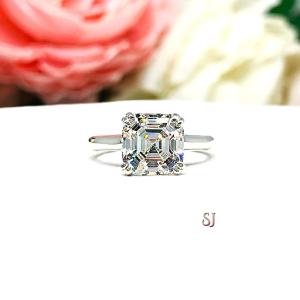 Sterling silver 8mm near colorless (G/H color) asscher cut cubic zirconia solitaire engagement ring. The ring is resting on a white surface with a background of pink and white flowers.
