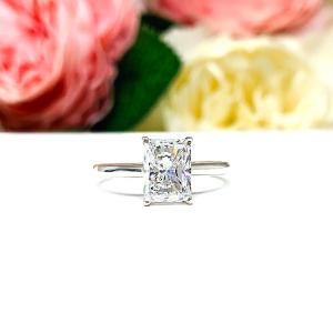 Elegant sterling silver cathedral engagement ring set with an 8x6mm radiant cut cubic zirconia, beautifully photographed against a romantic and timeless soft-focus floral background of pink and white blooms.