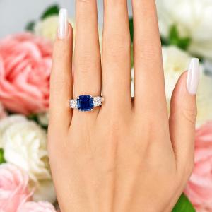 A woman's hand wearing a sterling silver ring featuring an elegant sterling silver 3-stone ring with a 10mm Asscher‑cut lab blue sapphire center and 6mm CZ side stones. Model image for size and styling reference — not a photo of the actual ring.