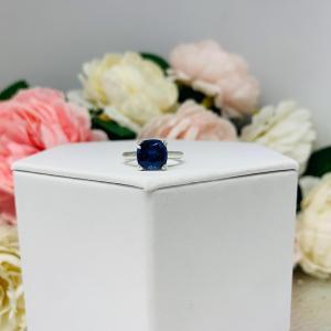 Unedited photo sterling silver cathedral-style ring featuring a 8mm cushion cut lab created blue sapphire center stone.  The ring is facing forward to showcase the mixed brilliant faceting and highly polished band.