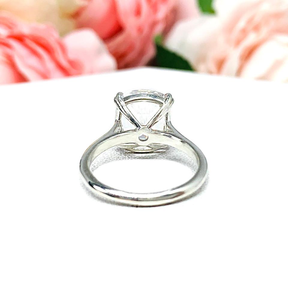 Sterling silver engagement ring featuring a sparkling elongated cushion-cut lab created white sapphire held in a split-prong setting, with soft-focus pink and white flowers in the background.