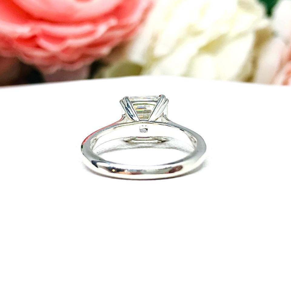 Sterling silver 8mm near colorless (G/H color) asscher cut cubic zirconia solitaire engagement ring. The ring is resting on a white surface with a background of pink and white flowers.