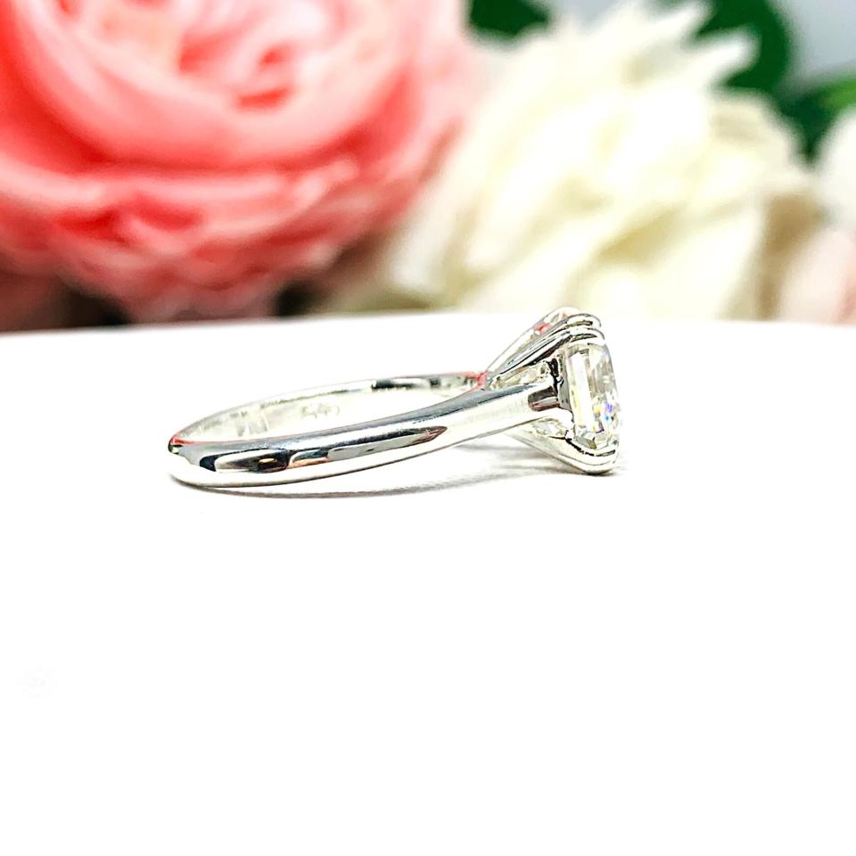 Sterling silver 8mm near colorless (G/H color) asscher cut cubic zirconia solitaire engagement ring. The ring is resting on a white surface with a background of pink and white flowers.