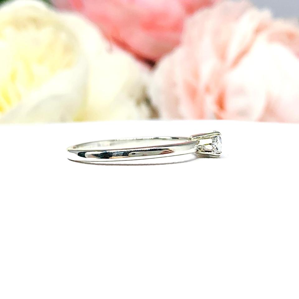 Dainty 4-prong sterling silver, horizontal east west set engagement ring featuring a precision-faceted marquise cubic zirconia.  Displayed on a white surface with soft pastel floral background.