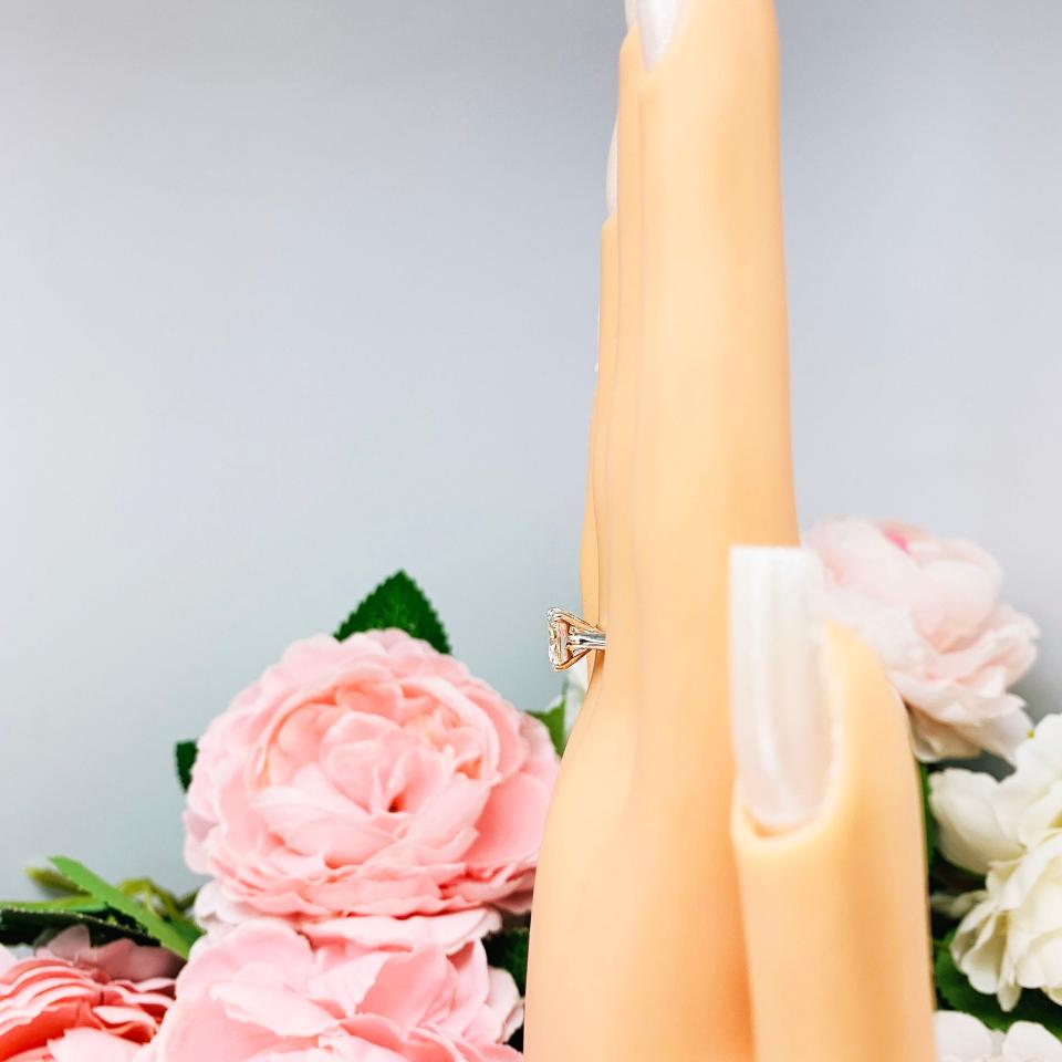 Mannequin hand with long white shimmery nails, displayed against a soft white-gray background with pink and white floral accents. The hand is wearing a sterling silver split prong cathedral engagement ring set with an 7.5mm near colorless old mine cut cubic zirconia.