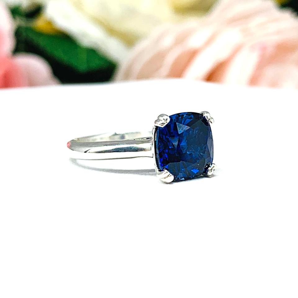 Close-up of a sterling silver cathedral-style ring featuring an 8mm cushion cut lab created blue sapphire center stone. The ring is facing slightly to the right to showcase the mixed brilliant faceting and highly polished band.