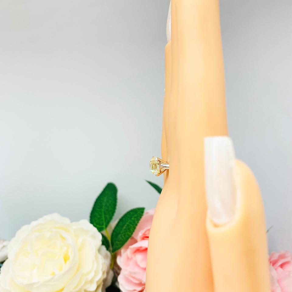 Mannequin hand with long white shimmery nails, displayed against a soft white-gray background with pink and white floral accents. The hand is wearing a sterling silver split prong cathedral engagement ring set with an 8mm light yellow old mine cut cubic zirconia.