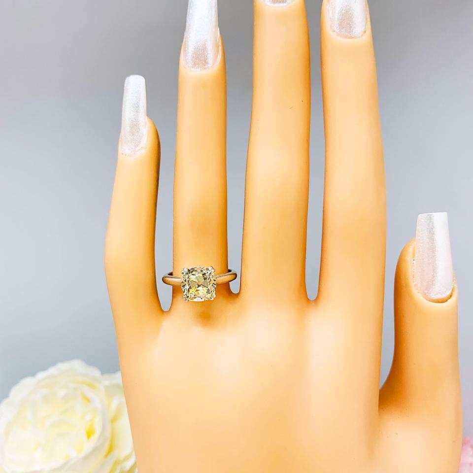 Mannequin hand with long white shimmery nails, displayed against a soft white-gray background with pink and white floral accents. The hand is wearing a sterling silver split prong cathedral engagement ring set with an 8mm light yellow old mine cut cubic zirconia.
