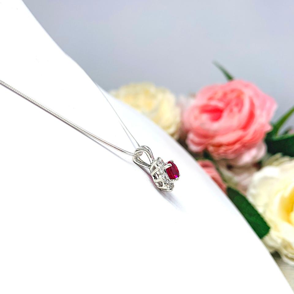 Sterling silver halo pendant necklace featuring a round vivid deep red lab ruby center stone (5mm–8mm), surrounded by small CZs in a floral-inspired setting on a delicate silver chain.