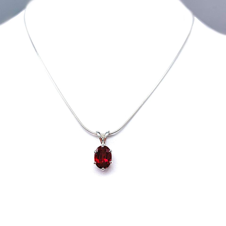 Sterling silver necklace featuring an oval lab-created ruby pendant in a six-prong setting, suspended from a thin silver chain and photographed against a white background.