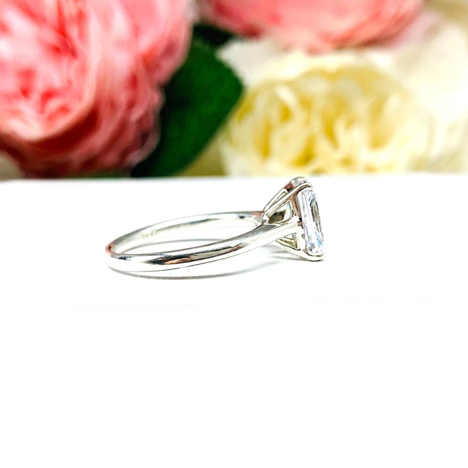 Elegant sterling silver cathedral engagement ring set with an 8x6mm radiant cut cubic zirconia, beautifully photographed against a romantic and timeless soft-focus floral background of pink and white blooms.