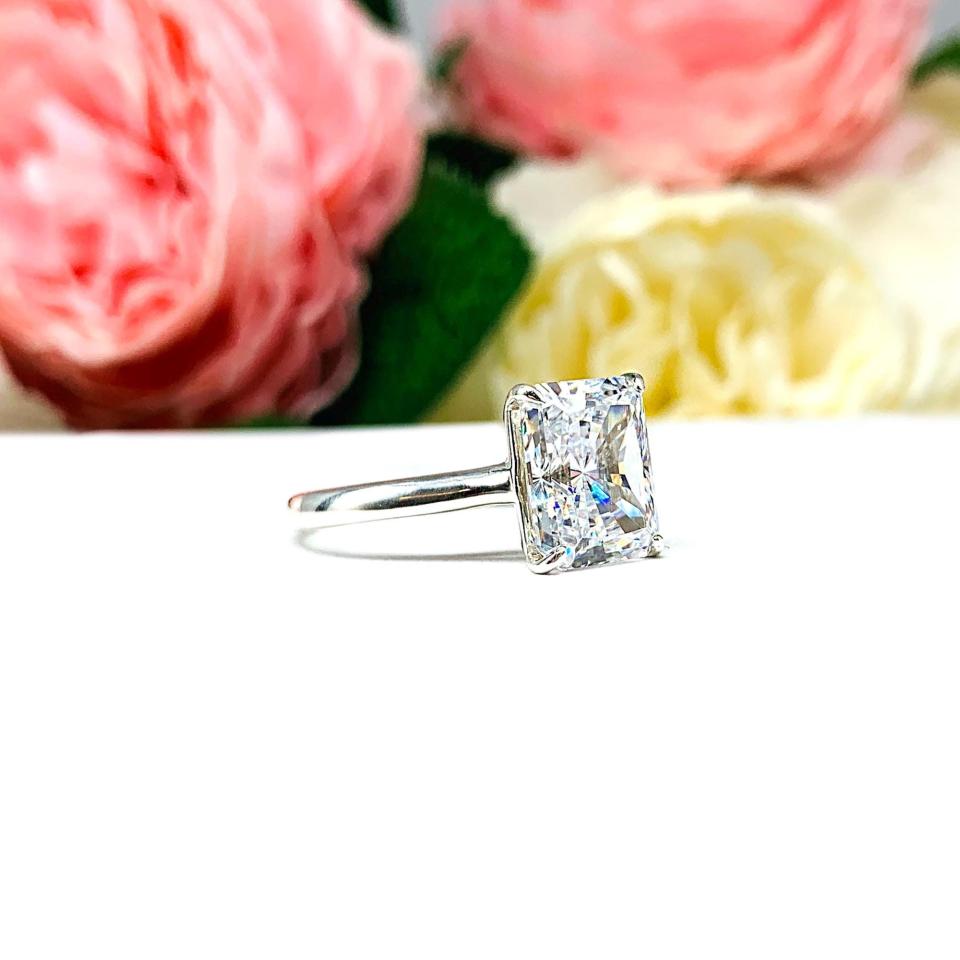 Elegant sterling silver cathedral engagement ring set with a 10x8mm radiant cut cubic zirconia, beautifully photographed against a romantic and timeless soft-focus floral background of pink and white blooms.