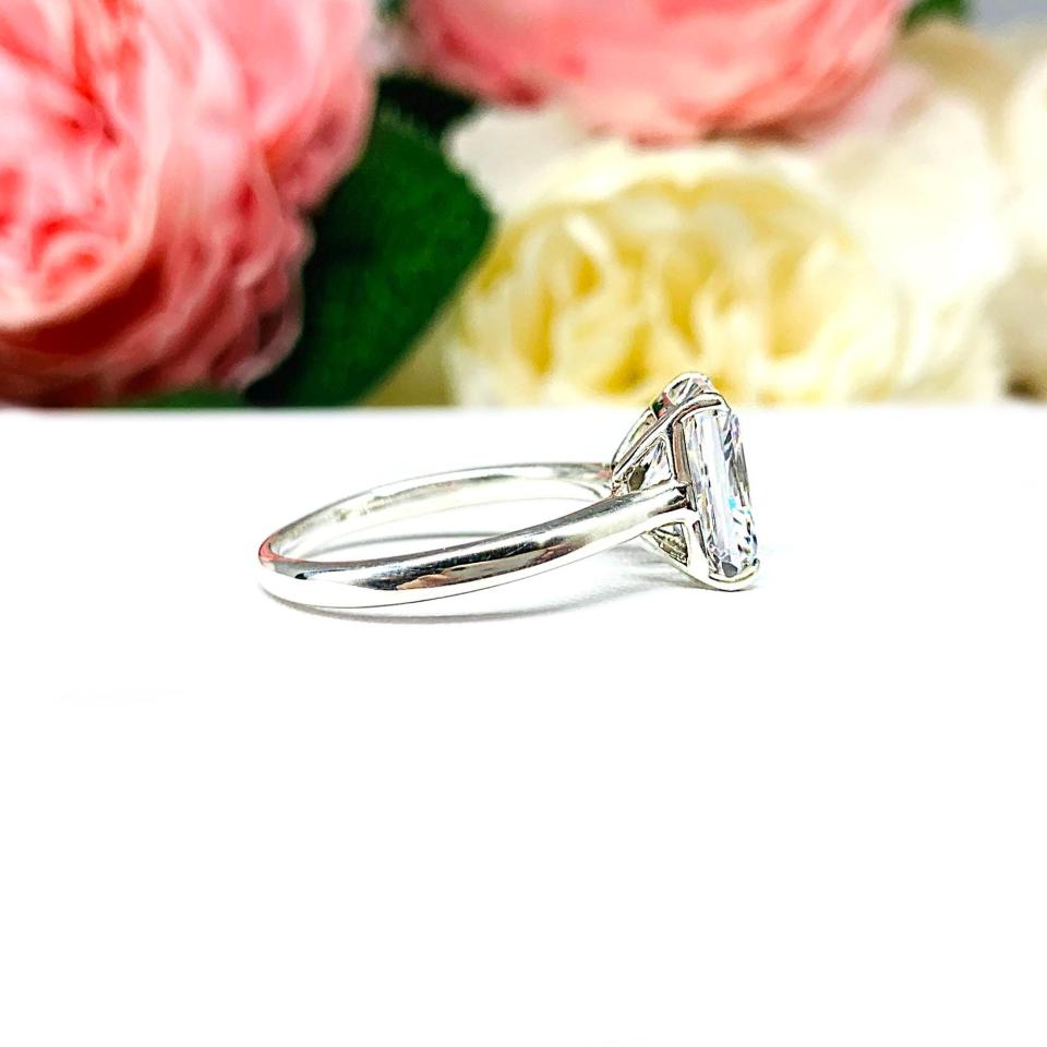 Elegant sterling silver cathedral engagement ring set with a 10x8mm radiant cut cubic zirconia, beautifully photographed against a romantic and timeless soft-focus floral background of pink and white blooms.