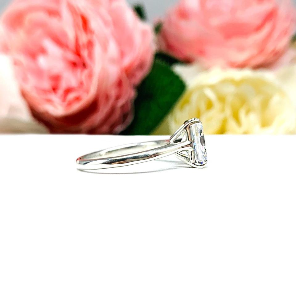 Elegant sterling silver cathedral engagement ring set with a 9x7mm radiant cut cubic zirconia, beautifully photographed against a romantic and timeless soft-focus floral background of pink and white blooms.