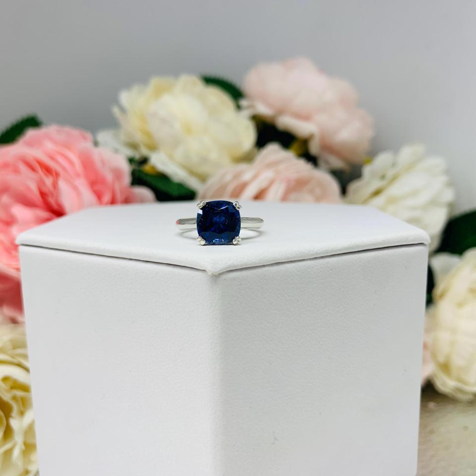 Unedited photo sterling silver cathedral-style ring featuring a 8mm cushion cut lab created blue sapphire center stone.  The ring is facing forward to showcase the mixed brilliant faceting and highly polished band.