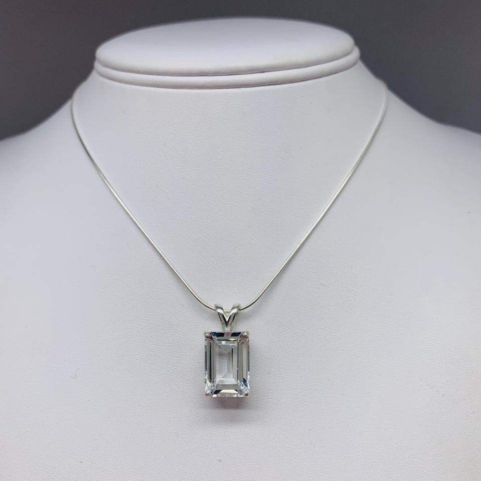 Unedited photo of an emerald-cut white topaz pendant necklace featuring a faceted natural gemstone in a sterling silver prong setting, suspended from a delicate sterling chain. Available in five stone sizes.