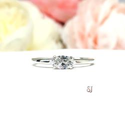 Dainty 4-prong sterling silver, horizontal east west set engagement ring featuring a precision-faceted marquise cubic zirconia.  Displayed on a white surface with soft pastel floral background.