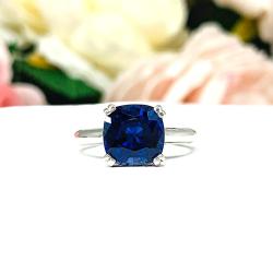 Close-up of a sterling silver cathedral-style ring featuring an 8mm cushion cut lab created blue sapphire center stone.  The ring is facing forward to showcase the mixed brilliant faceting and highly polished band.
