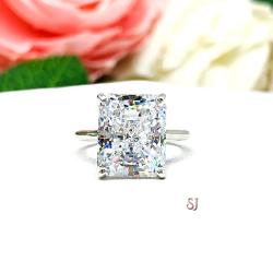 Elegant sterling silver cathedral engagement ring set with a large radiant cut cubic zirconia, beautifully photographed against a romantic and timeless soft-focus floral background of pink and white blooms.